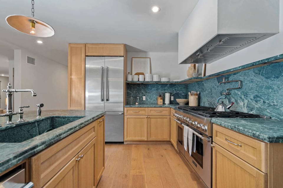 Full chef's kitchen — professional range with custom hood, green marble backsplash, and stainless French-door refrigerator