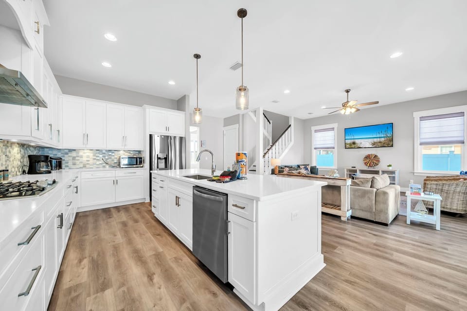 White shaker cabinets, pendant lights over a chef's island, and a clear view straight to the living room — this kitchen keeps the cook in the conversation.