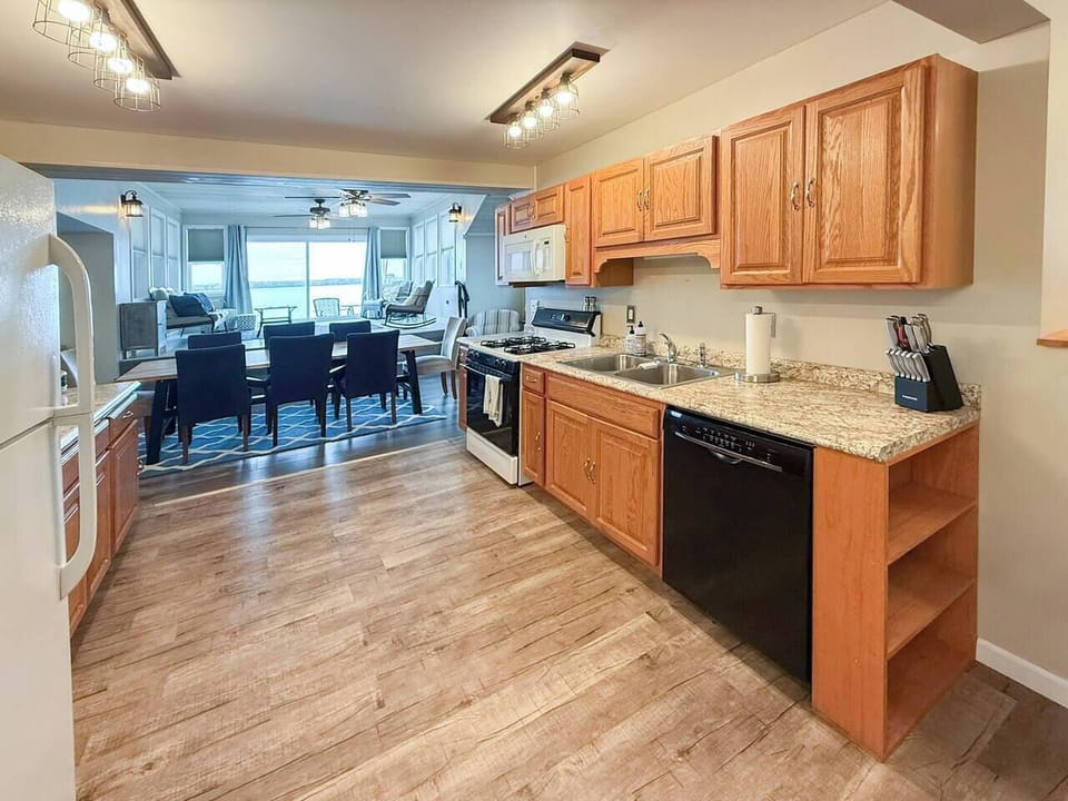 A fully equipped kitchen with gas range, dishwasher, and granite counters — open to the dining room with Cayuga Lake visible straight ahead. Cook together, eat together, stay together.
