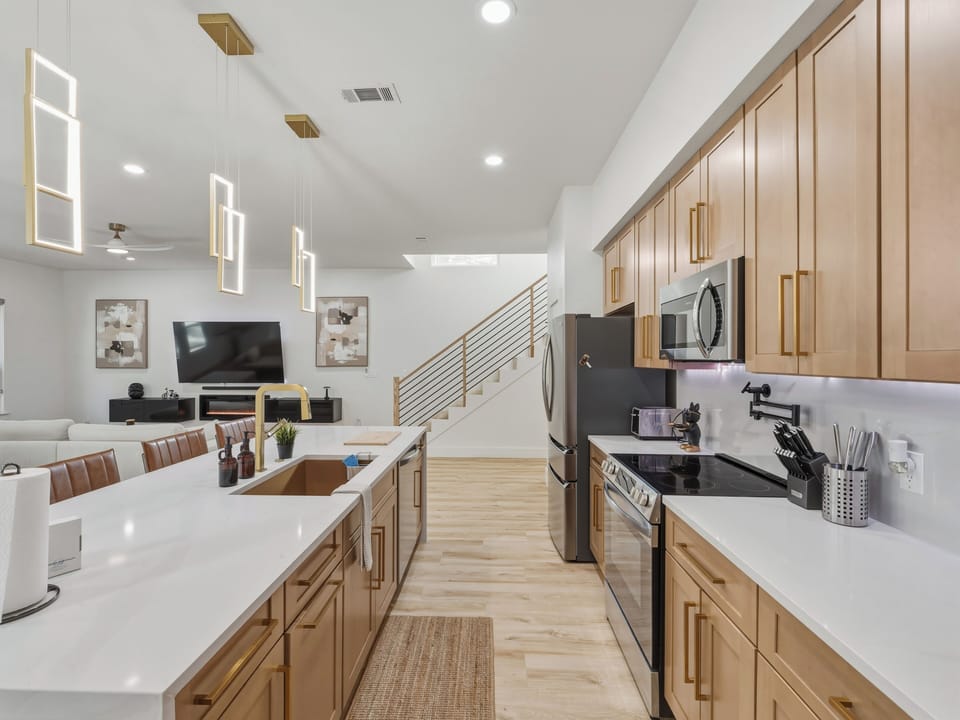 Your modern kitchen flows seamlessly into the living area, featuring sleek countertops, stainless steel appliances, and warm wood cabinetry—perfect for preparing meals while staying connected with your group.