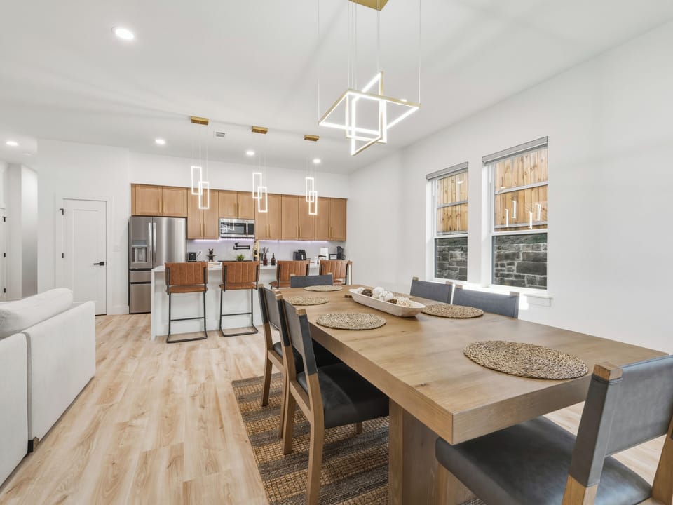 Picture yourself gathering around this stunning dining table with your group, bathed in natural light streaming through tall windows. The open layout connects you seamlessly to the modern kitchen, perfect for shared meals and conversation.
