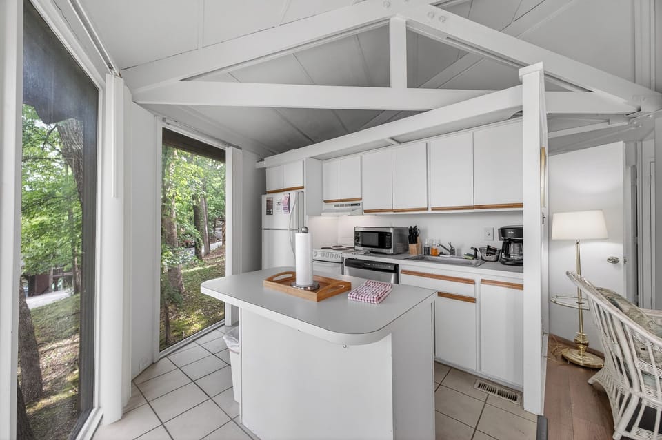 Your bright kitchen invites you to prepare meals with nature views through large glass doors that frame the surrounding trees and garden.