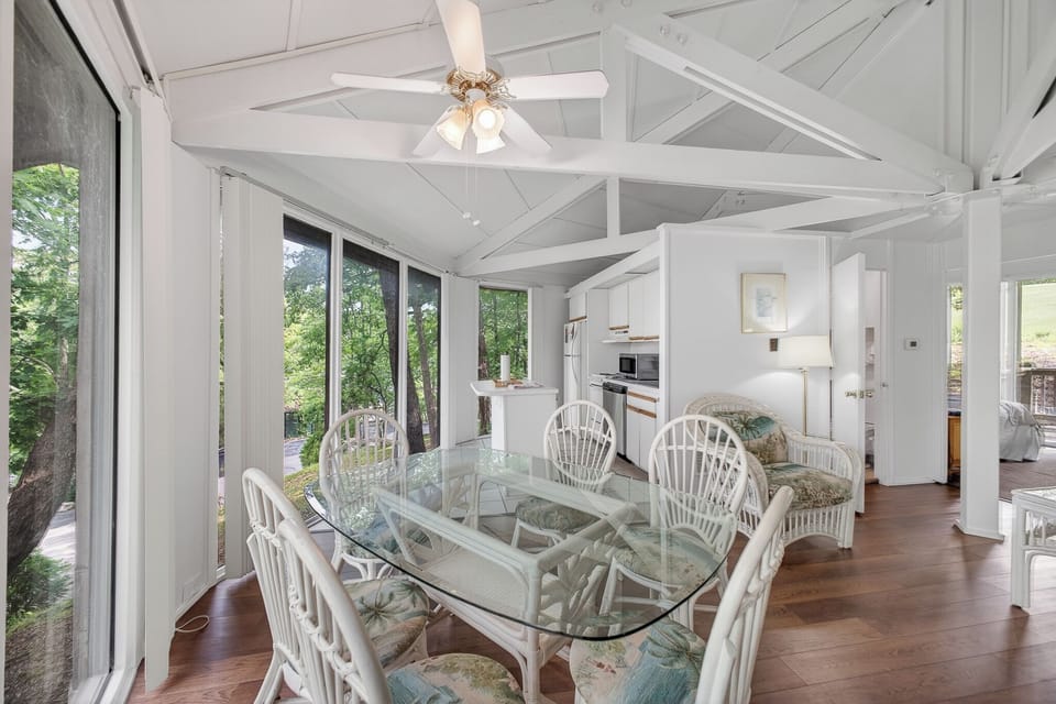 Gather around the elegant glass dining table for memorable meals, where cathedral ceilings and large windows bring the lush forest views indoors. The open-concept space flows seamlessly into the fully equipped kitchen, perfect for your vacation retreat.