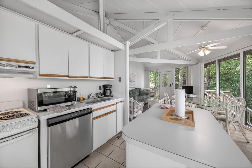 Your bright, fully-equipped kitchen flows into a cozy living space framed by large windows overlooking lush greenery, perfect for preparing meals while staying connected to nature.