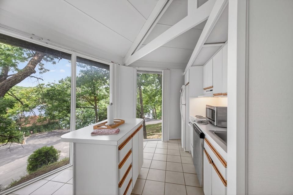 Enjoy cooking in this bright galley kitchen, where floor-to-ceiling windows frame peaceful lake views and fill your space with natural light.