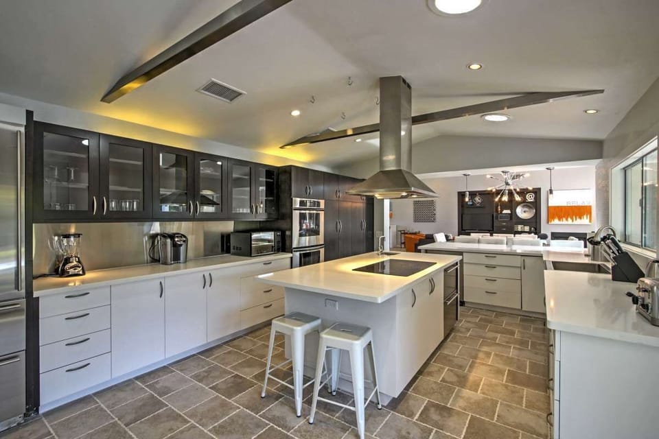 Spacious kitchen with a central island and bar stools, two-tone cabinetry, stainless appliances, and stone-tile flooring, open to the living areas.