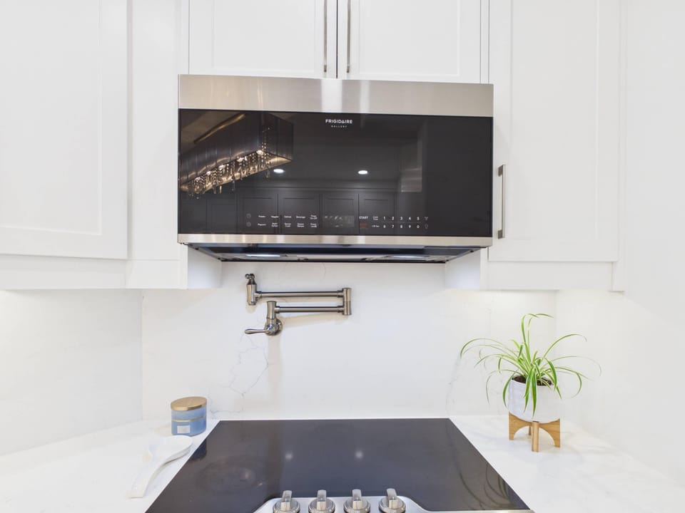 Sleek black and stainless steel microwave hood above a black cooktop, set against white cabinetry and marble countertops.