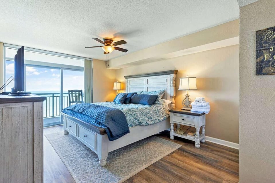 Whitewashed wood bed with blue patterned bedding faces sliding glass doors opening to an ocean-view balcony.
