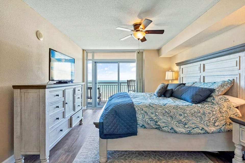 King bed with patterned blue bedding faces sliding glass doors opening to an ocean-view balcony.