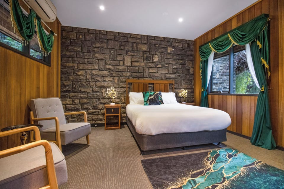 Cozy lodge-style bedroom with stone wall, plush bed, and garden views