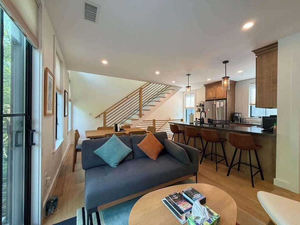 The open-riser staircase connects the floors in style — the kitchen peninsula and pendant lighting are visible just beyond the second-floor living area.