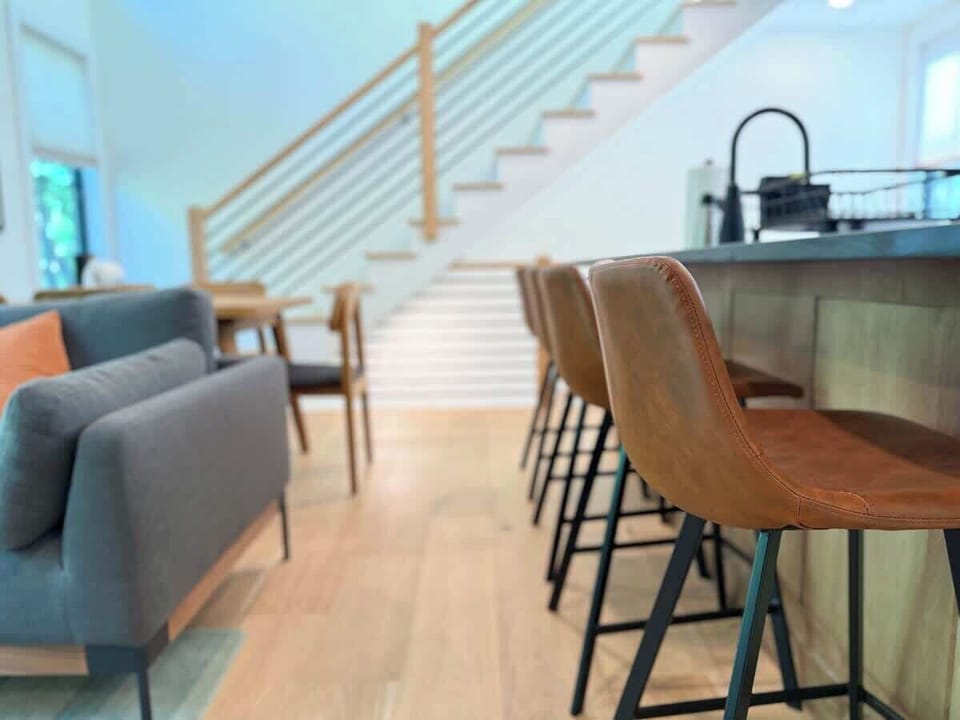 The peninsula bar seating for four sits at the base of the open-riser staircase — a natural spot for morning coffee or keeping the cook company.