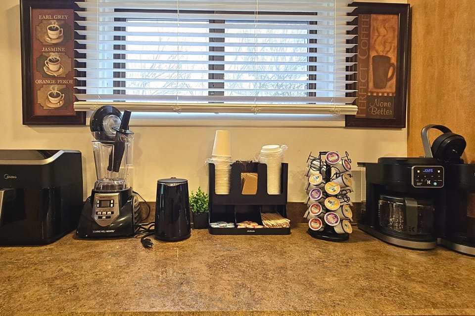 Stocked coffee bar: K-cups, drip brewer, kettle, blender & supplies.