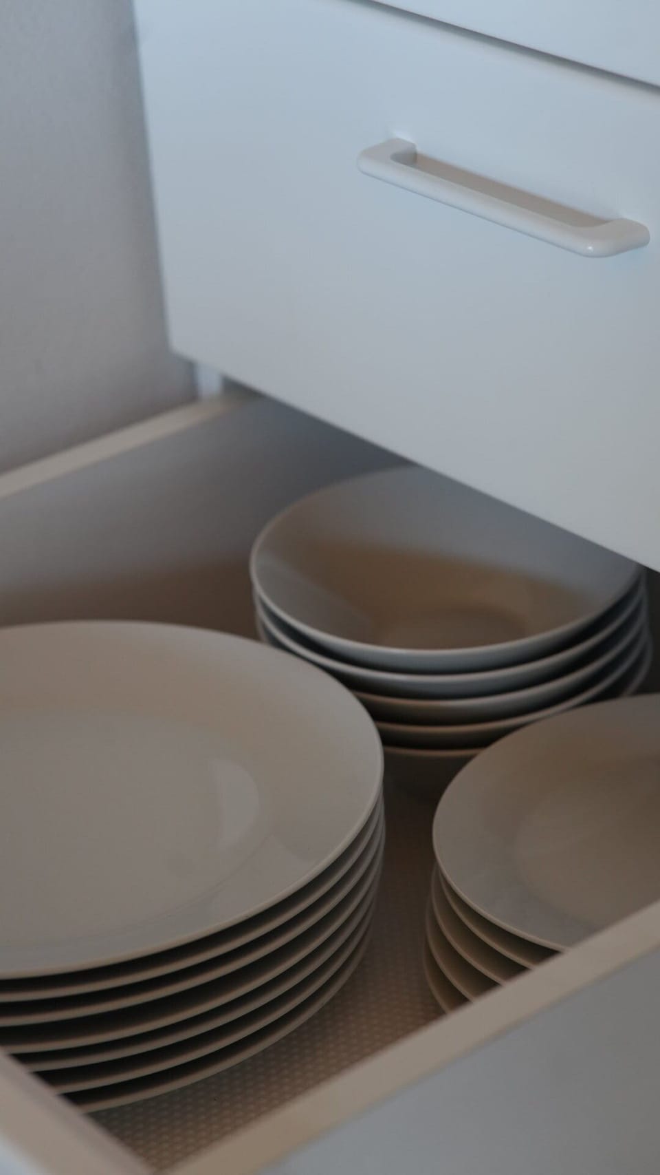 A clean stack of ceramic plates and bowls inside the kitchen cabinet for guests.