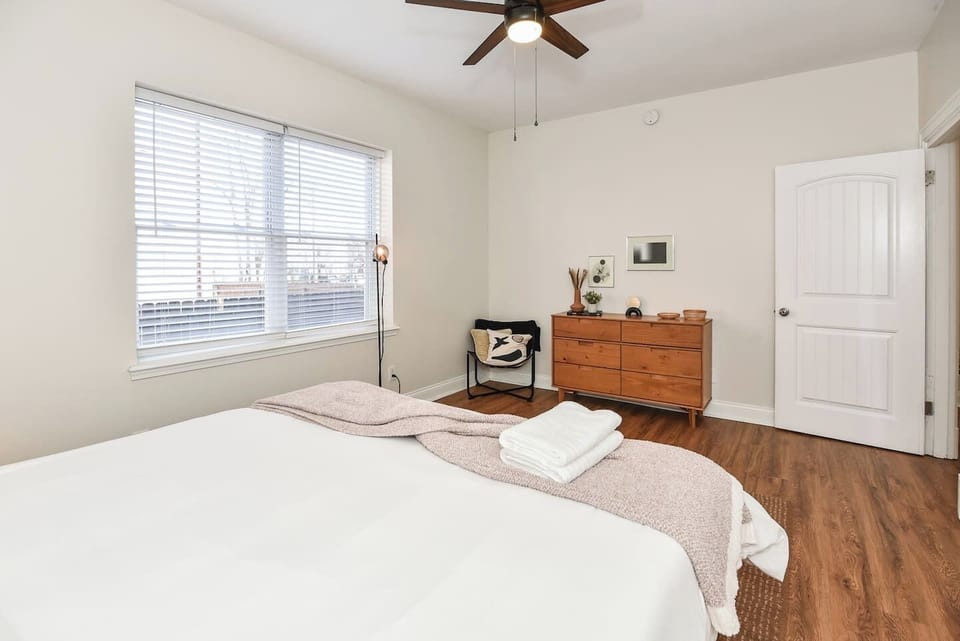 Bedroom with large windows, dresser storage & chair. 