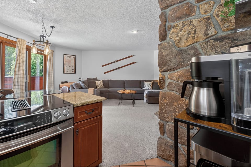 Relax on your spacious sectional sofa in this cozy living area, complete with a rustic stone accent wall and fully-equipped kitchen, perfect for mountain getaways.