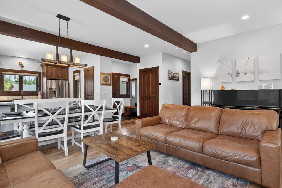 Relax in your open-concept living space with rustic wood beams overhead, a plush leather sofa, and a dining area that flows seamlessly into the modern kitchen—perfect for gathering.