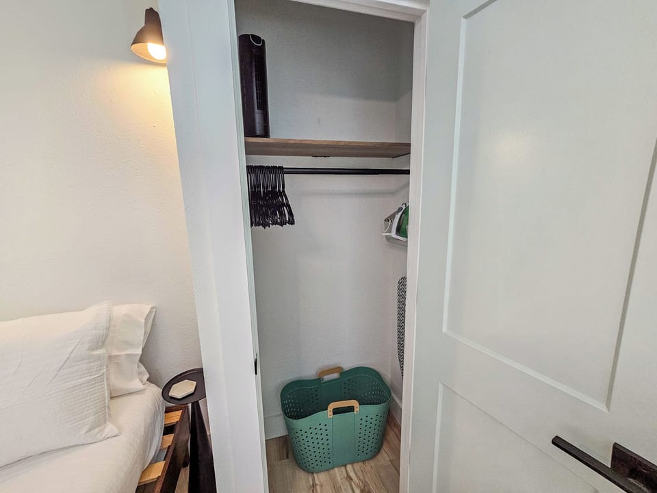 Convenient bedroom closet with hangers, laundry basket, iron & ironing board.