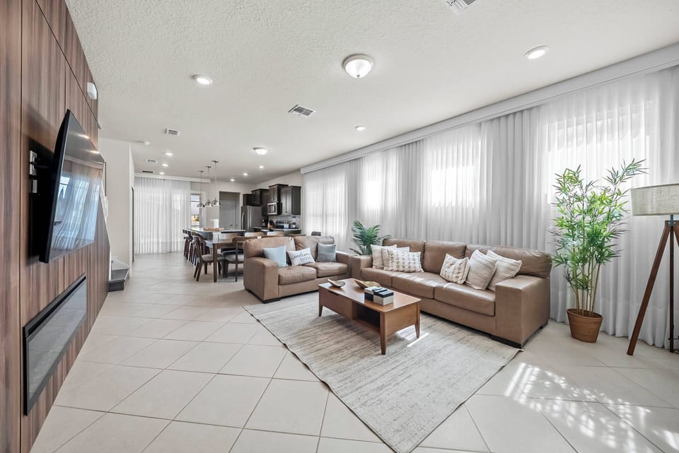 Welcome to a bright living area filled with natural light from large windows. Relax on the cozy sectional sofa with elegant throw pillows, surrounded by stylish wooden accents and a soft area rug for added warmth.