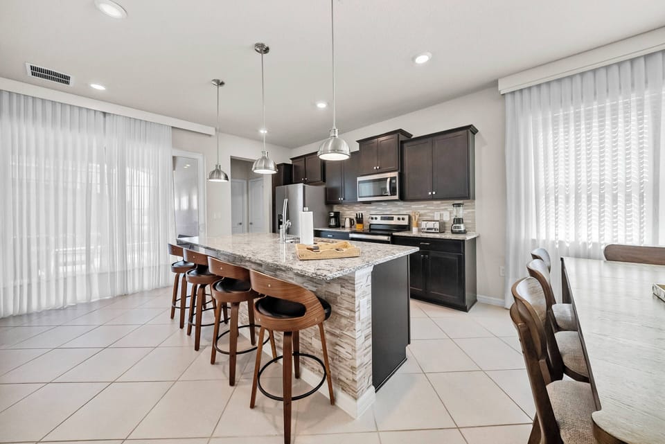 Enjoy a beautifully designed kitchen featuring sleek dark cabinetry and a spacious island with stylish bar seating. Natural light flows through sheer curtains, creating an inviting atmosphere for your culinary adventures.