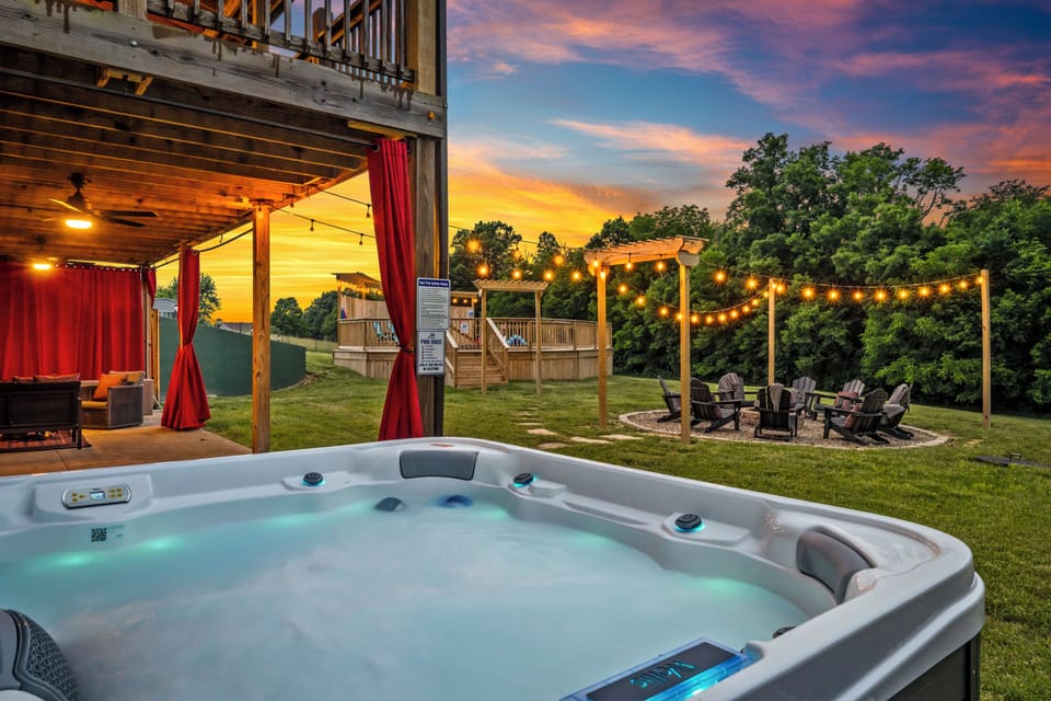 Private hot tub, fire pit, and string-lit yard at sunset. Firewood available for guests to use