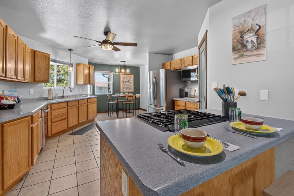 Kitchen island with gas cooktop and place settings overlooks oak cabinetry and tiled floor.