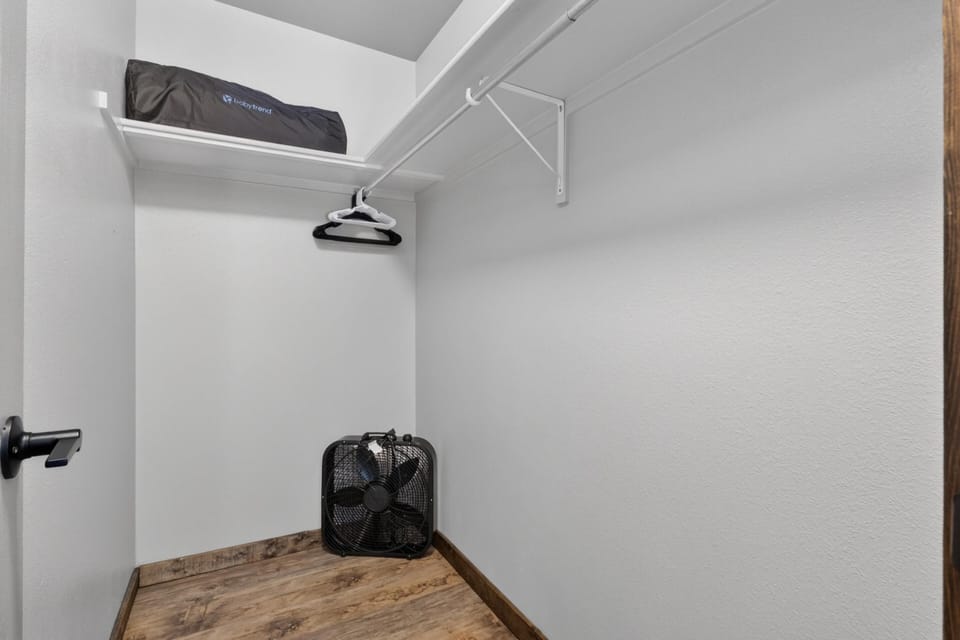 Empty closet corner with wood-look vinyl flooring, white walls, and a black box fan on the floor.