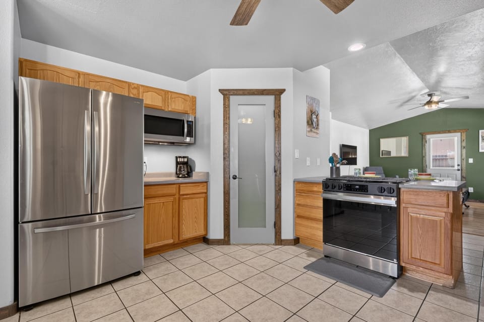 Kitchen corner with stainless steel refrigerator, oak cabinets, tiled floor, and frosted glass pantry door.