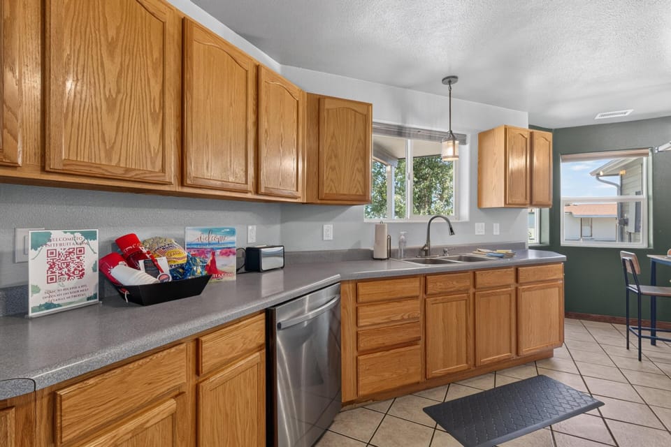Oak cabinetry lines the kitchen walls above and below gray laminate countertops with a stainless steel dishwasher.