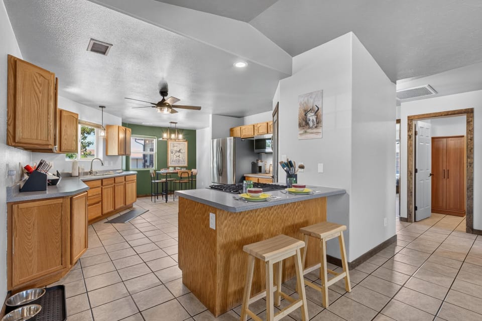 Kitchen features oak cabinetry, tiled flooring, a gray countertop island with two wooden stools, and a green accent wall.