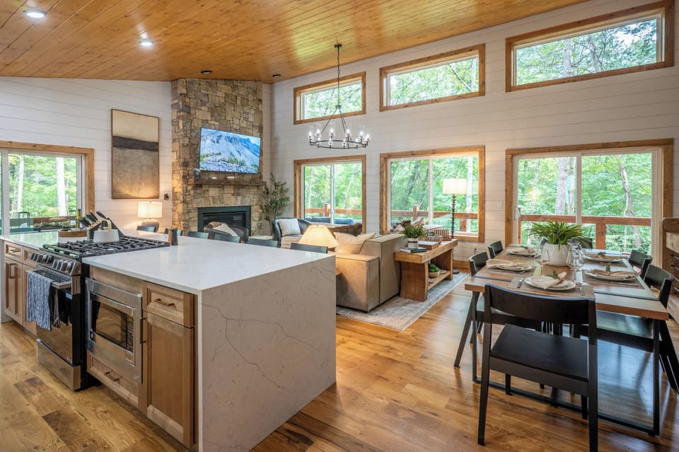 Bright open living space with stone fireplace and peaceful forest views