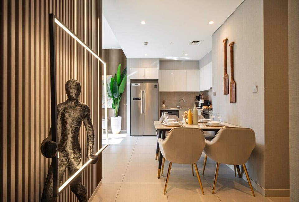 Elegant dining area featuring a stylish four-seat dining table, beautiful statement lighting, and aesthetic décor. Conveniently located next to the fully equipped kitchen and refrigerator, creating the perfect space for dining and gathering.