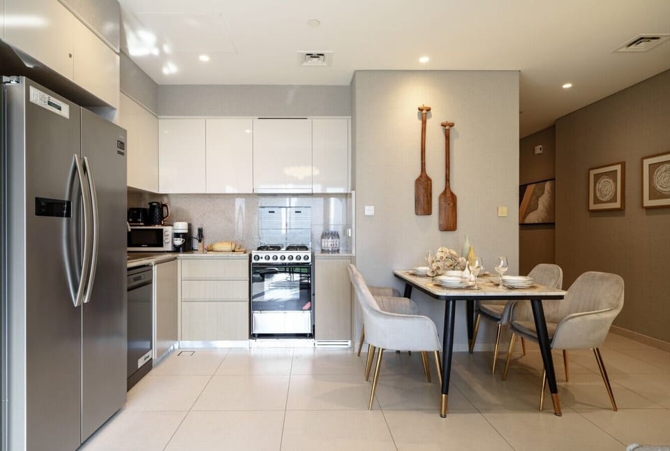 Modern kitchen and dining area featuring a dining table with comfortable seating, a large refrigerator, oven, microwave, electric kettle, and dishwasher. Fully equipped for preparing meals and enjoying a convenient, home-like stay.