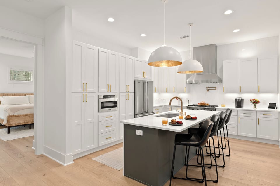 Gourmet kitchen showcasing a massive quartz island with a breakfast bar, under-mount sink, and contemporary dome pendant lighting.