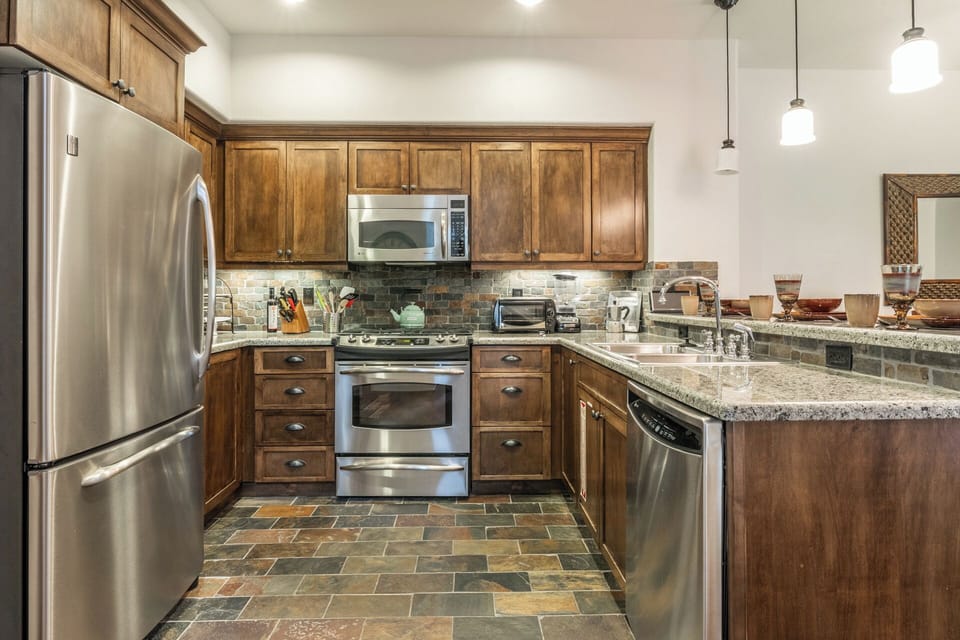 Your fully-equipped kitchen features warm wood cabinetry, granite countertops, and stainless appliances—perfect for preparing meals at home. Enjoy the cozy ambiance of the stone tile floors and pendant lighting.
