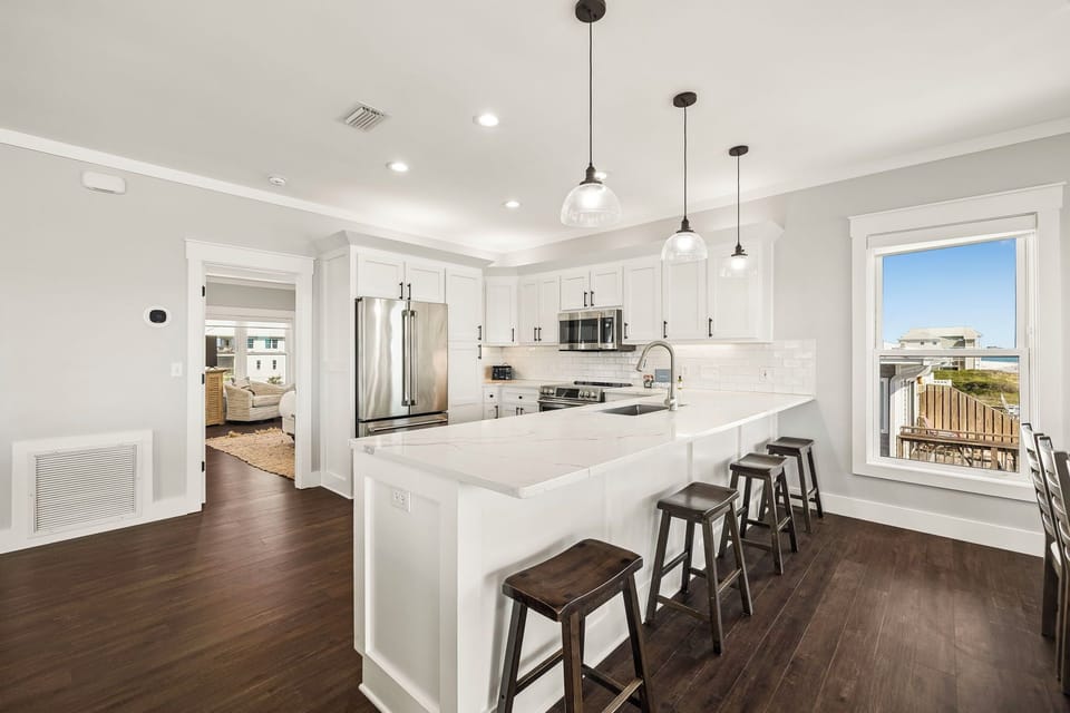 Step into a bright, contemporary kitchen where rich wood floors meet crisp white cabinetry. Gather at the spacious island with seating for everyone, and enjoy stunning views beyond.
