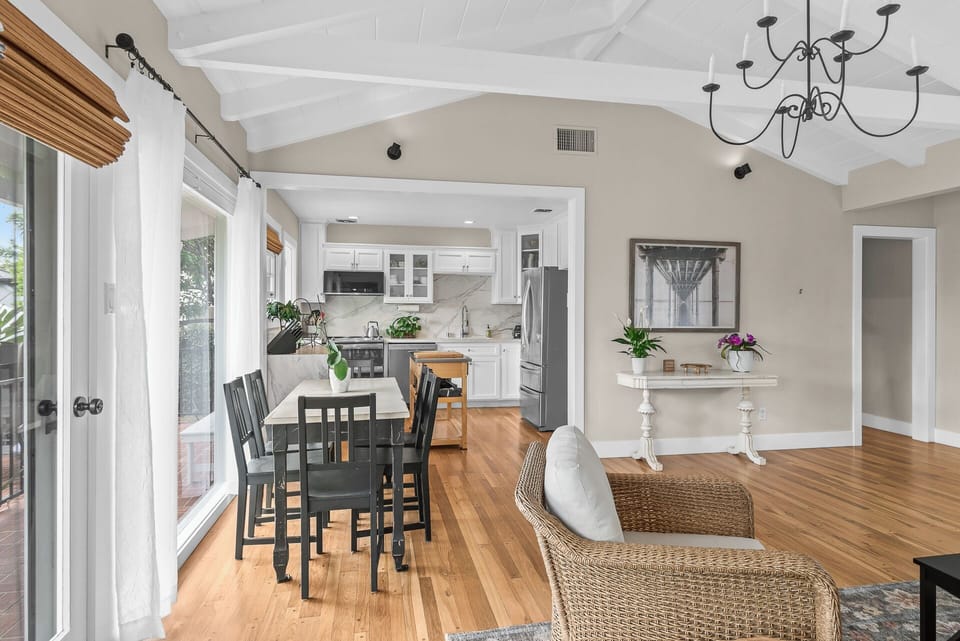 Gather and unwind in the open-concept living and dining area, featuring vaulted ceilings, abundant natural light, comfortable seating, a smart TV, and easy access to the outdoor patio.