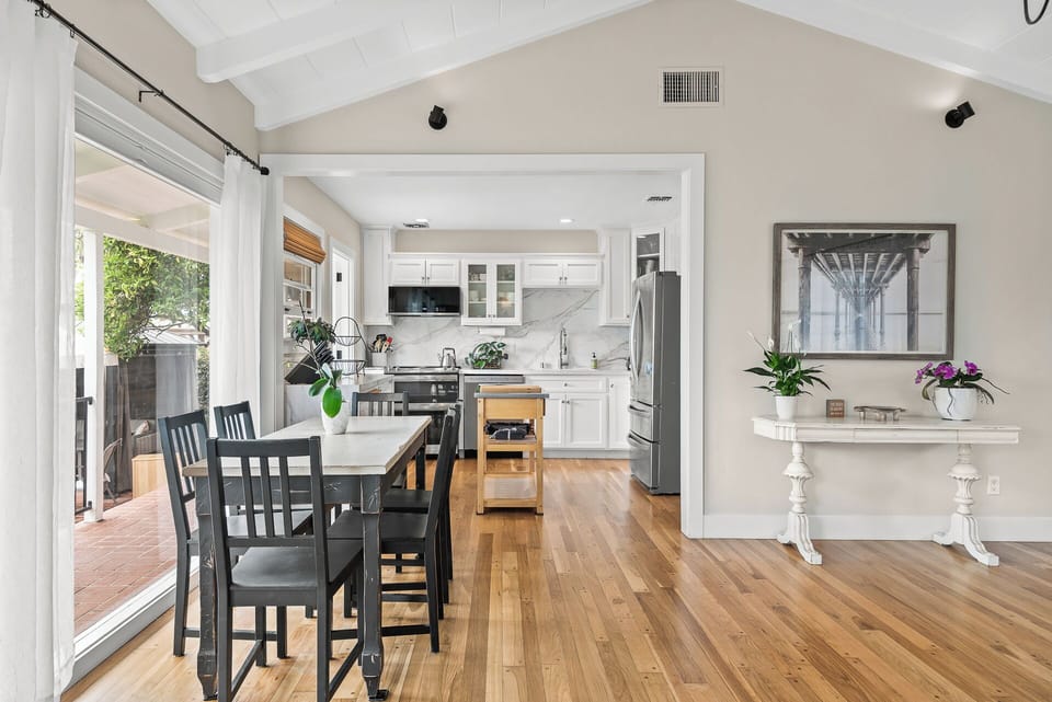 Gather and unwind in the open-concept living and dining area, featuring vaulted ceilings, abundant natural light, comfortable seating, a smart TV, and easy access to the outdoor patio.
