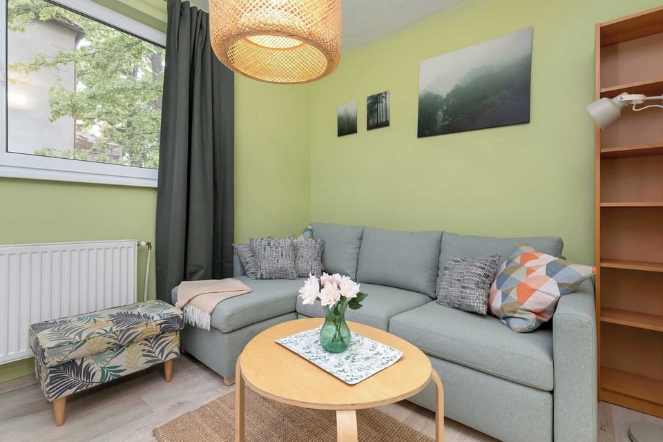 A cozy living room with a gray sofa, coffee table, and framed artwork on a pale blue wall. Large windows provide plenty of natural light.