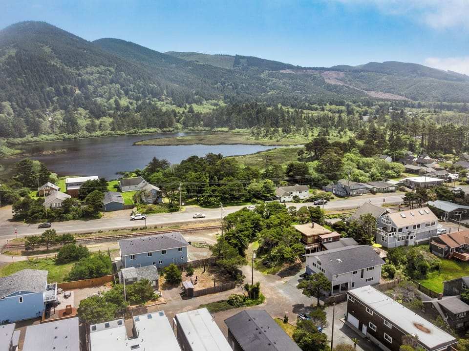 Aerial view of a coastal neighborhood nestled between forested mountains and a tranquil lake, offering scenic natural surroundings and outdoor recreation opportunities nearby.