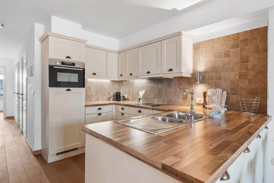 Fully equipped modern kitchen with white cabinetry, wood worktop, oven and microwave. Knokke vacation duplex.