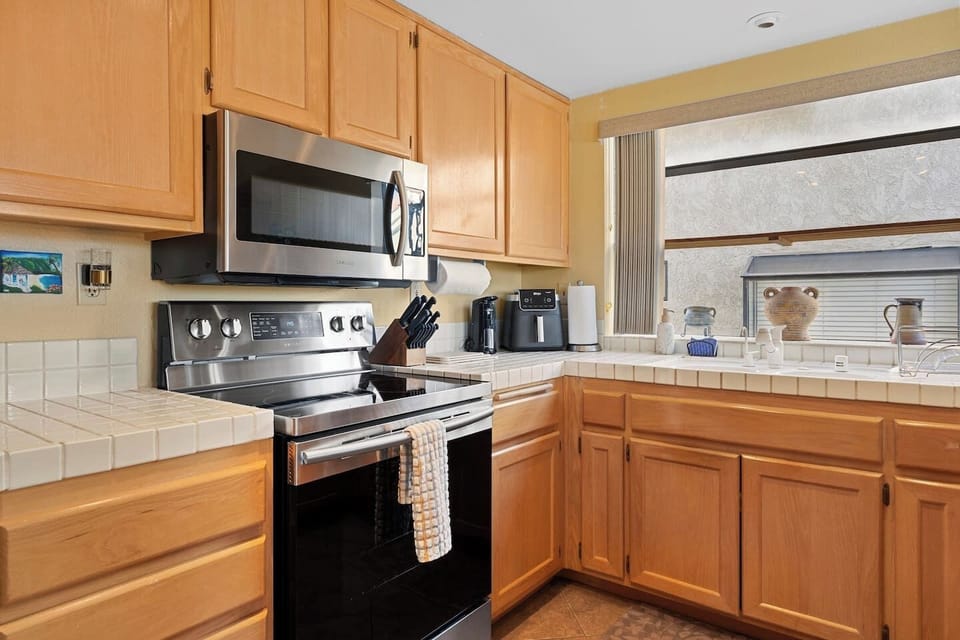 Well-equipped kitchen with stainless appliances, coffee maker, air fryer, and plenty of counter space, all filled with natural light