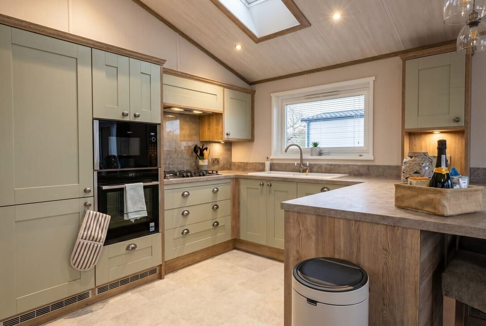 Sage green kitchen with skylight, double oven and gas hob for cooking.