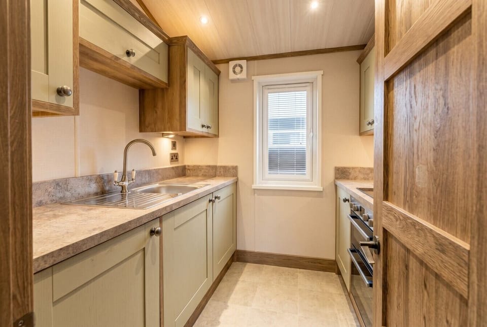 A neat galley kitchen with sage cabinetry and a double oven for easy cooking.