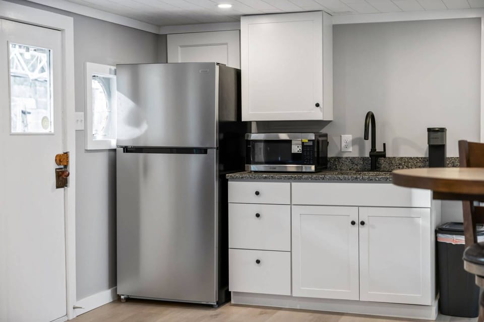 Kitchenette showing full-size stainless fridge, microwave, granite countertop, sink, and Keurig.