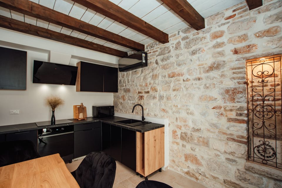 Air-conditioned kitchen with dining area, stone wall, wooden beams and modern equipment.