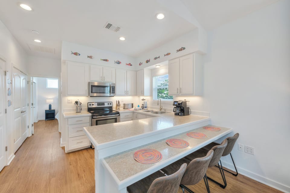 Gather around the spacious breakfast bar in your bright, fully-equipped kitchen, where gleaming countertops and modern appliances await your culinary adventures under charming coastal decor.