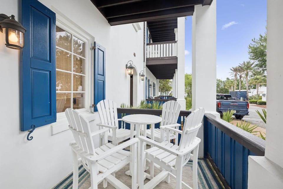 Balcony with white Adirondack chairs and round table on a striped blue and beige outdoor rug.