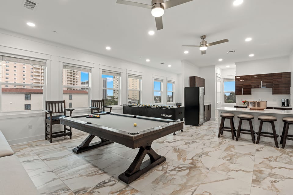 Spacious open-concept game room with a professional billiards table, foosball, and a bar area.