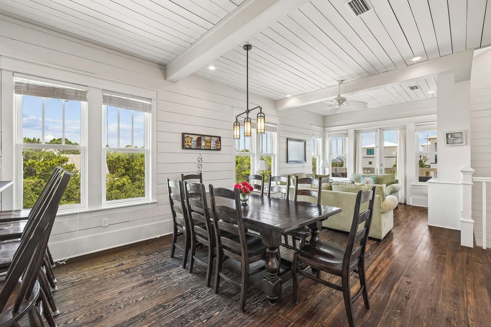 Gather around this spacious dining table where your family meals come with a side of coastal charm. Natural light floods in through large windows, framing lush greenery and inviting you to linger over breakfast or toast to another perfect beach day.